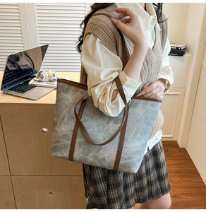Détail d'un sac cabas gris en daim avec poignées en cuir marron dans un bureau