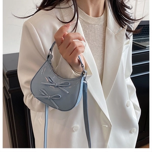 Détail du sac croissant en cuir verni bleu clair avec nœuds sur une veste de blazer blanche