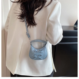 Détail du sac croissant bleu clair avec nœuds porté sur un blazer blanc chic