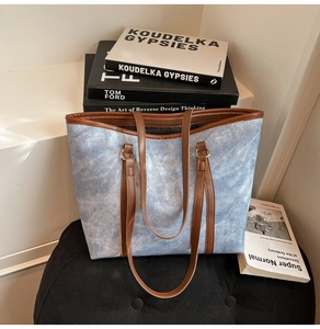Détail du sac cabas en denim bleu avec des anses en cuir marron sur un meuble moderne