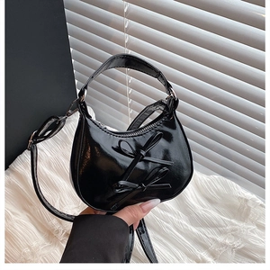 Détail du sac demi-lune noir brillant avec nœuds papillon et chaîne argentée