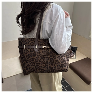 Close-up of leopard print tote bag with brown leather handles and golden metal buckles