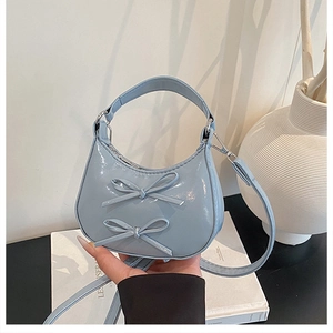 Détail du sac croissant en cuir verni bleu clair avec des nœuds décoratifs élégants