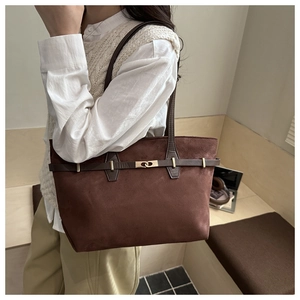 Close-up of a large brown suede tote bag with golden metal hardware on a female model