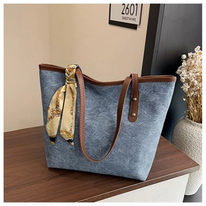Detail of blue denim tote bag with brown leather handles and a decorative silk scarf