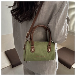 Modèle portant un sac Boston en suédine vert mousse avec des lanières en cuir marron