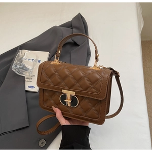 Detail of a brown quilted square handbag with gold T-bar buckle and smooth leather handle