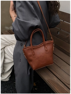 Vue détaillée du grain de litchi marron et du logo doré sur le sac seau en similicuir