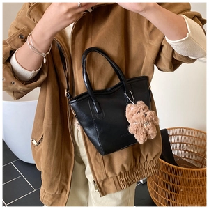 Détail d'un sac seau en similicuir noir avec un charmant pendentif ours en peluche sur l'épaule