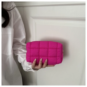 Detail of rose red quilted makeup bag with gold zipper held by a model