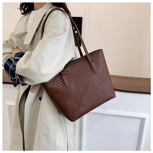 Brown woven tote bag on shoulder with light trench coat for daily casual style