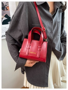 Glossy red crossbody bag with top handle and gold logo shown on model for sizing
