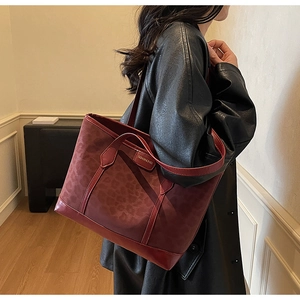 Detail of dark red leopard print tote bag with metal label and wide shoulder strap
