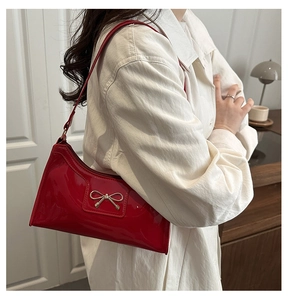 Détail du sac bandoulière en cuir verni rouge avec boucle nœud doré porté par un mannequin