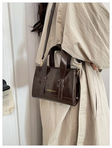 Detailed side view of a glossy dark brown crossbody square bag with gold lettering