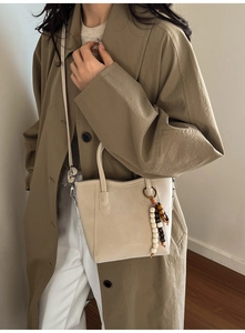 Detail of beige bucket bag with wooden bead charm and embossed texture on PU leather