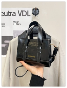 Macro detail of glossy black structured box bag with Fashion & Bags text and handle