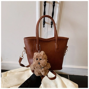 Détail d'un sac seau en similicuir marron avec poignées et pendentif chien en peluche