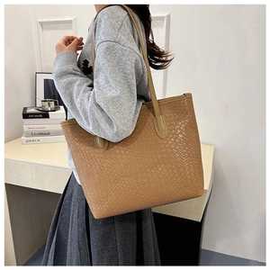 Close-up of woven texture and long handles on a tan tote bag held by a model