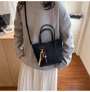 Detail of minimalist black suede tote bag with decorative wooden bead tassel pendant