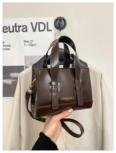 Macro detail of dark brown polished leather handbag with gold lettering and strap
