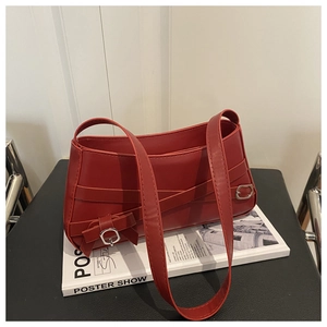 Close-up of red leather bag with cross straps and silver metal buckles on white book