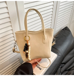 Detail of beige bucket bag featuring a beaded charm and embossed fashion text