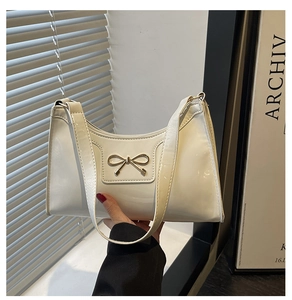 Detail of white glossy underarm bag featuring a golden bow metal buckle on premium leather