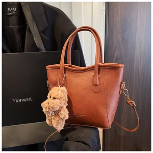 Détail du sac seau en cuir marron avec poignées, bandoulière et pendentif chiot en peluche