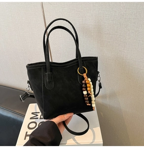 Detail of black suede bucket bag with cylindrical handles and ethnic beaded pendant charm