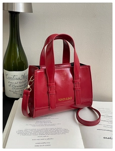 Detail of red glossy faux leather crossbody bag with gold FASHION & BAGS lettering