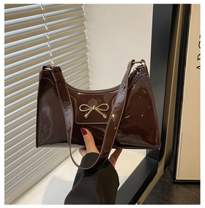 Detailed macro view of the glossy brown patent leather bag with a golden bow buckle