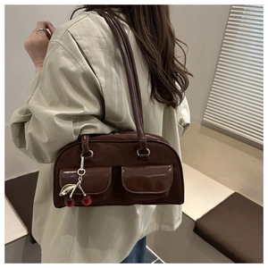 Detail of dark brown shoulder bag with double pockets and a cherry charm on model