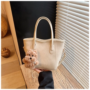 Détail du sac seau en cuir blanc cassé avec texte tendance et pendentif ours mignon