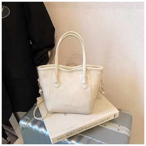 Détail du sac seau blanc crème avec texture cuir et ferrures dorées sur des livres