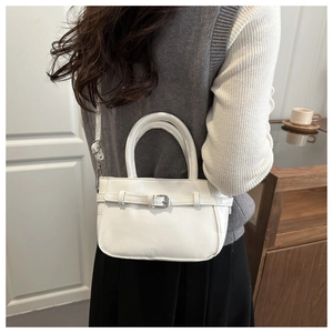 Chic white square crossbody bag with decorative buckle shown in a lifestyle street setting