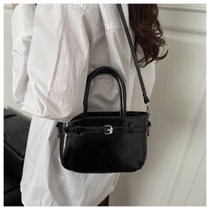Detail of black glossy leather handbag featuring silver buckle and dual carrying options