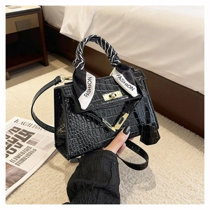 Detail of black crocodile texture handbag with gold lock and decorative fashion scarf