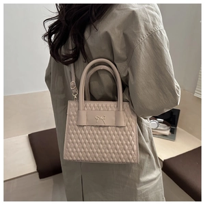 Beige quilted handbag with golden bow detail shown on a model for scale and style