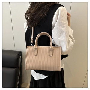 Detail of light beige tote bag featuring vertical stripes and a sleek metal buckle