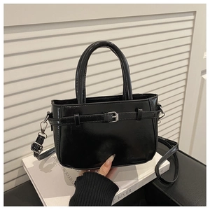 Close-up of black glossy crossbody bag with belt buckle detail on a white book