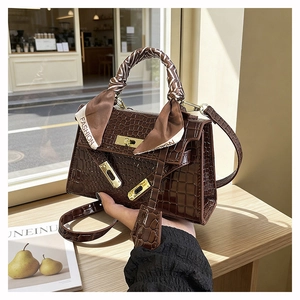 Macro shot of dark brown crocodile textured handbag with metallic clasp and silk scarf