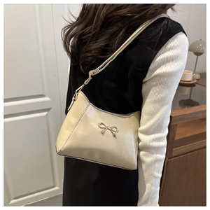 Detail view of cream leather shoulder bag with a gold bow buckle on female model