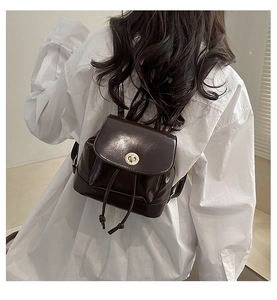 Detail of vintage brown glossy leather backpack with gold metal buckle on white shirt