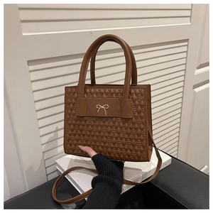 Detailed view of brown quilted leather handbag featuring a gold bow and sturdy top handles