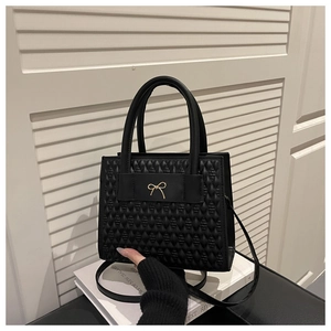Detail of black embossed geometric handbag with gold bow buckle on white book display