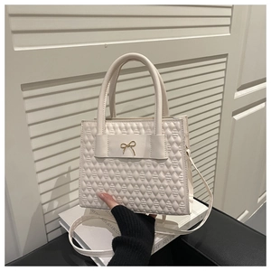 Détail du sac à main beige matelassé avec nœud doré et texture en cuir synthétique