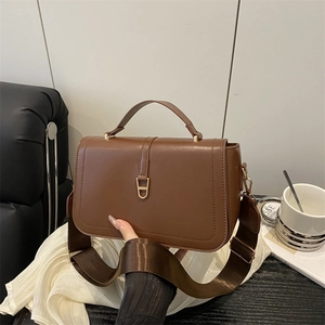 Brown PU leather shoulder bag with gold D-ring hardware and wide strap in lifestyle setting