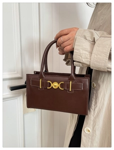 Detail of dark brown tote bag featuring gold heart buckle and fine leather texture