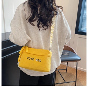 Detail of yellow corduroy crossbody bag with TOTE BAG embroidery and woven strap